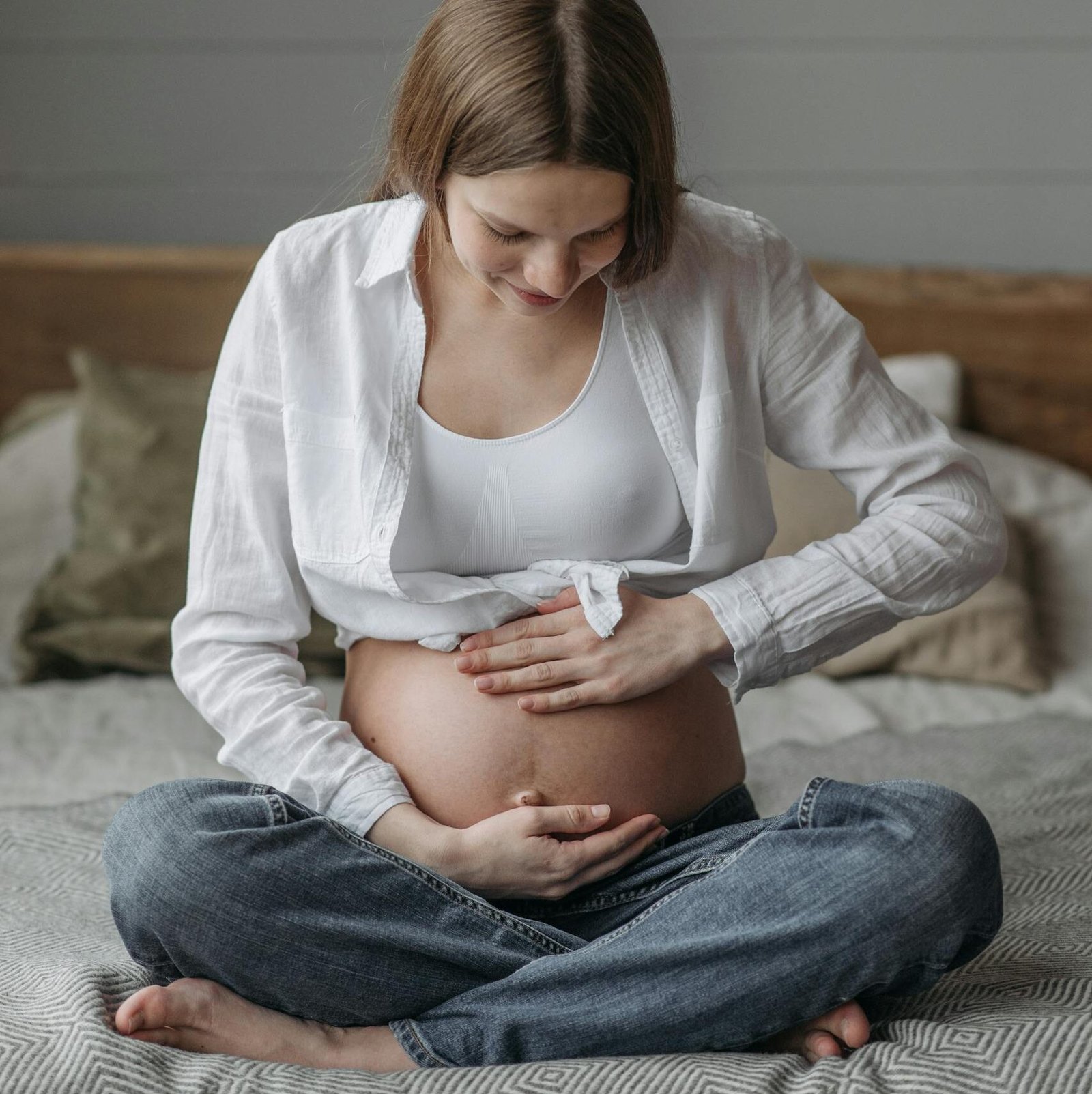 A serene portrait of a pregnant woman sitting on a bed, gently holding her baby bump.