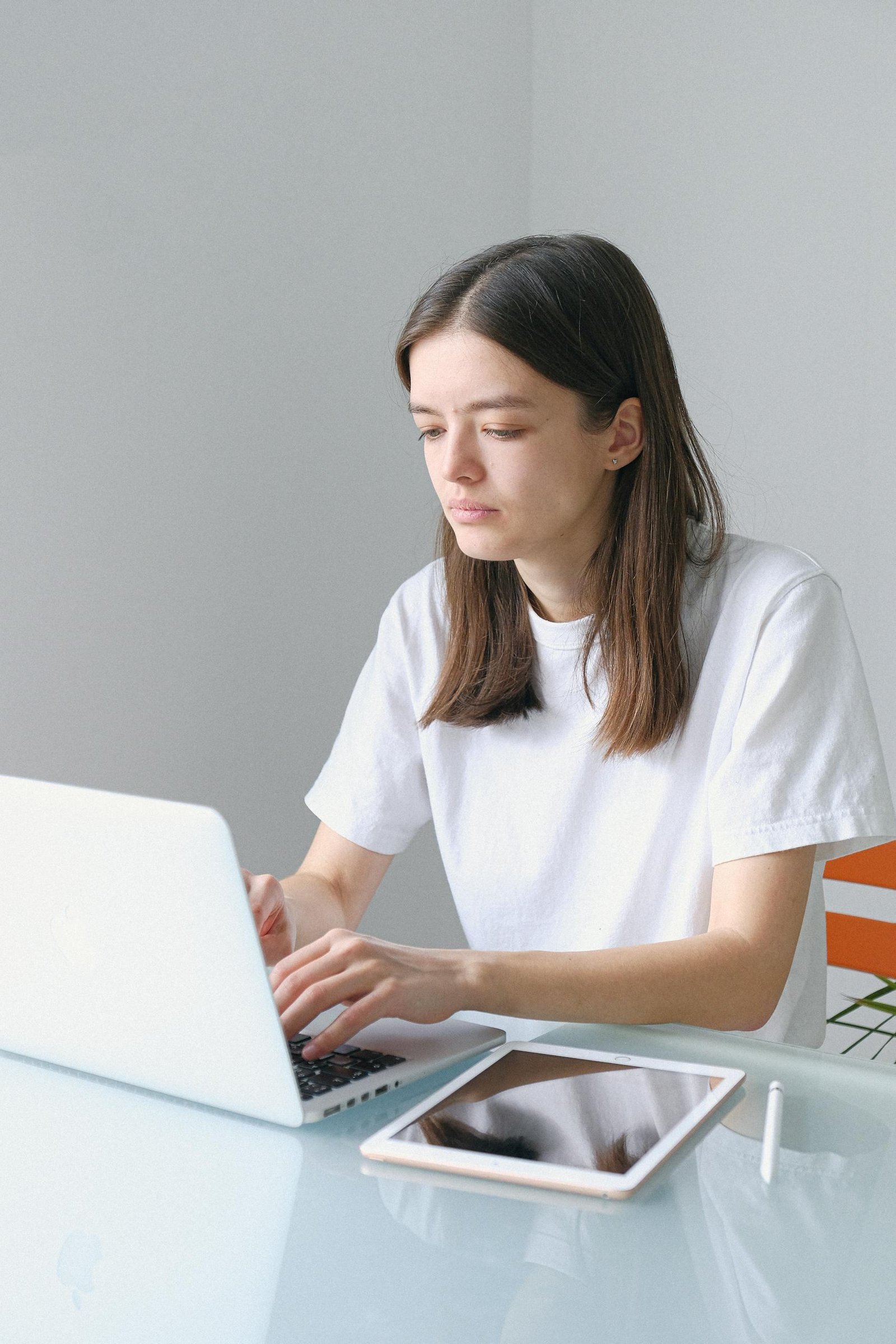 Young woman using a laptop and tablet at home office, symbolizing modern freelance work culture.
